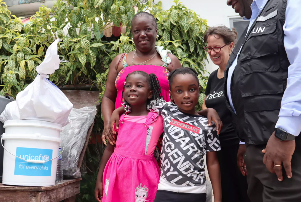 unicef beryl response photo with three adults and two children standing beside a bucket of hygiene items