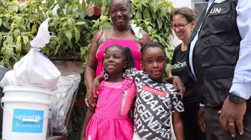 unicef beryl response photo with three adults and two children standing beside a bucket of hygiene items